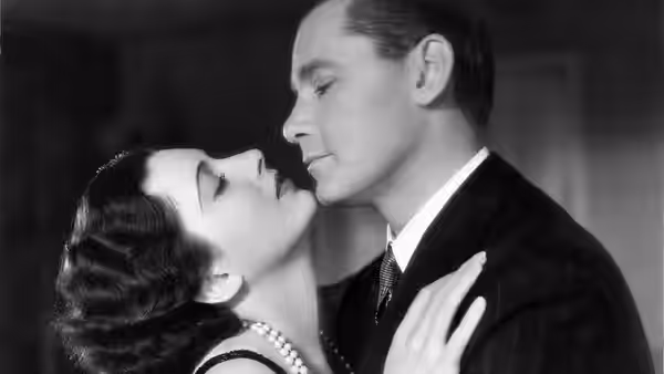 Gaston (Herbert Marshall) leans close to Lily (Miriam Hopkins) as she touches his chest