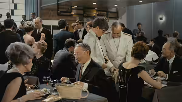 Restaurant patrons dine at crowded tables while waiters serve food and drinks