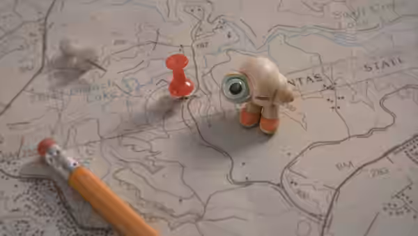 Marcel standing on a map beside a pencil and push pins