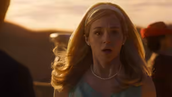 a blonde woman wearing a pearl necklace looking forward with surprise