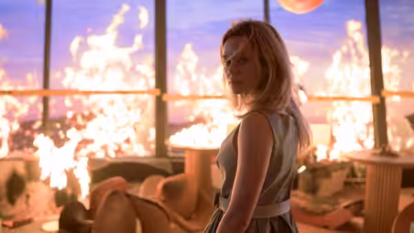 a woman in a dress standing in a room overlooking a fire