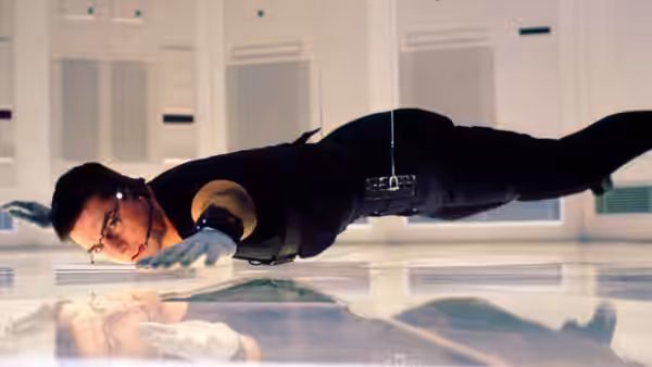 Ethan Hunt (Tom Cruise) reaching down while suspended above a reflective floor in a secure facility