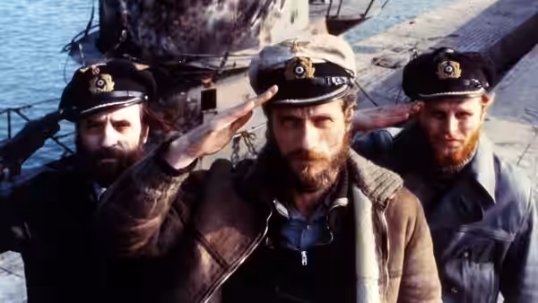 Three officers in naval caps stand on a ship's deck, one saluting