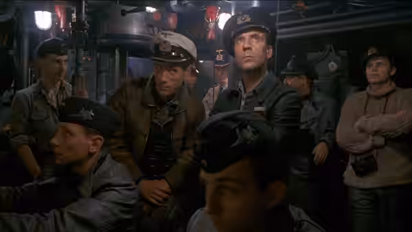 Crew members gather in a submarine compartment, watching with concern