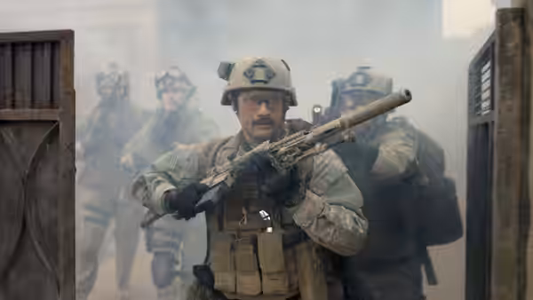 Soldier with a mustache holding a rifle in front of others amid smoke