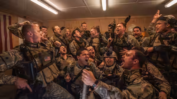 Group of soldiers in camouflage cheering and shouting inside a wooden room