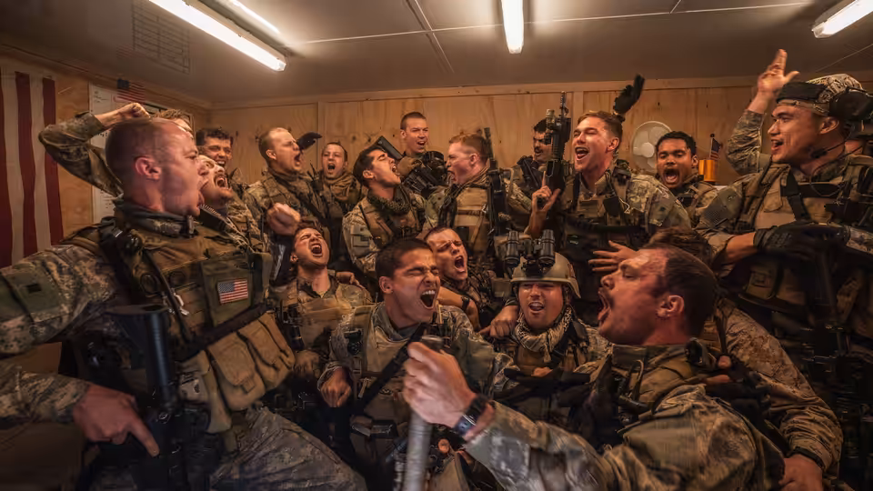 Group of soldiers in camouflage cheering and shouting inside a wooden room