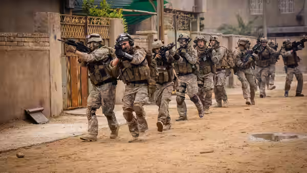 Armed soldiers in tactical gear running down a dusty street while aiming rifles