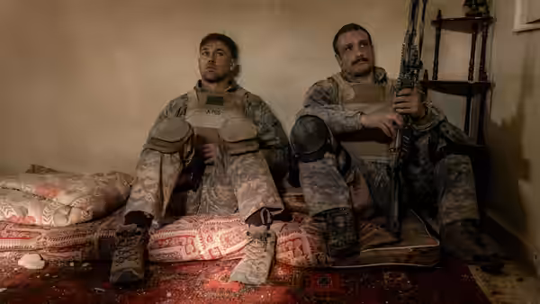 Two soldiers resting on mattresses against a wall in a sparse room