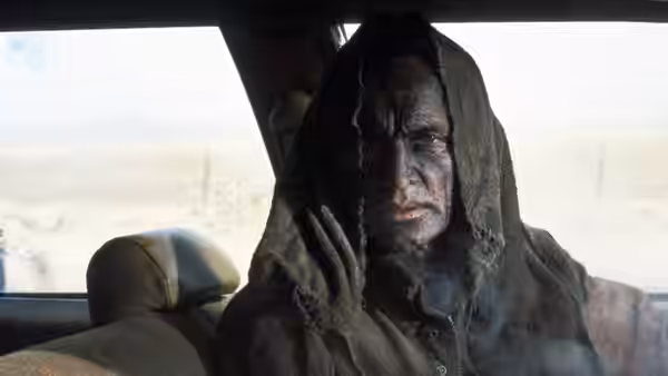 Jesse Hooker (Lance Henriksen) sits hooded inside a car