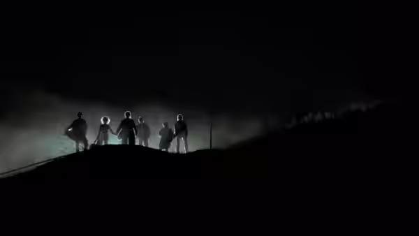 A group of figures stands silhouetted along a ridge in drifting fog