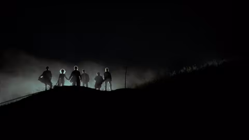 A group of figures stands silhouetted along a ridge in drifting fog