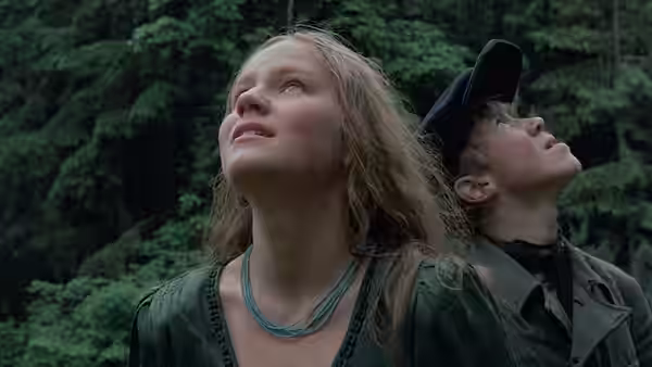 Glasha (Olga Mironova) and Flyora gazing upwards in a dense forest