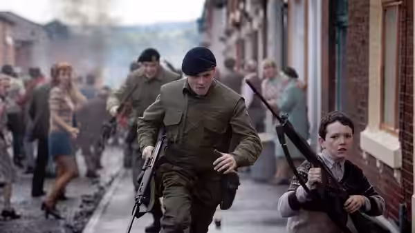 Gary Hook (Jack O'Connell) advances along a street holding a rifle, boy alongside