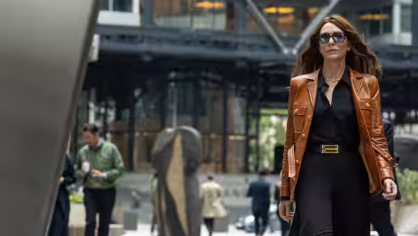 Woman in brown leather jacket walking through a modern plaza