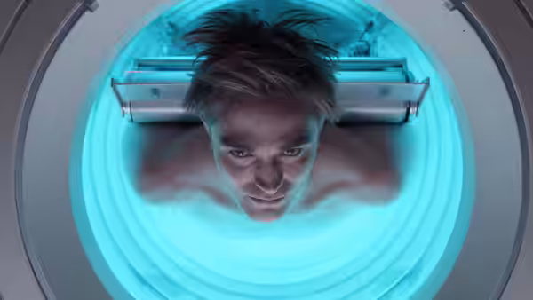 Mickey Barnes (Robert Pattinson) lying in a glowing blue scanner