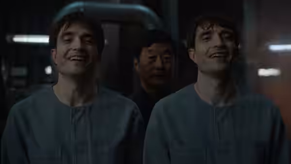 Two versions of Mickey Barnes (Robert Pattinson) smiling in gray uniforms