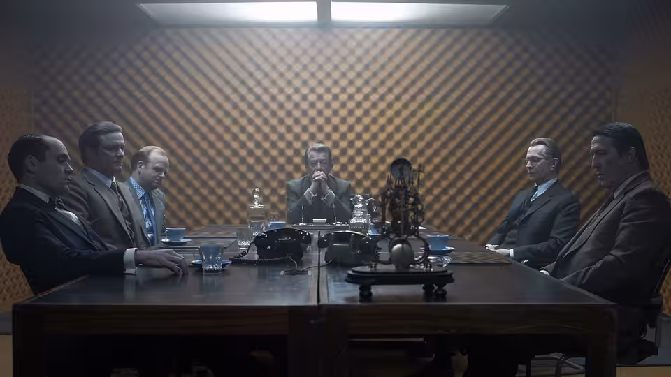 A group of men in suits gathered around a wooden table in a meeting room