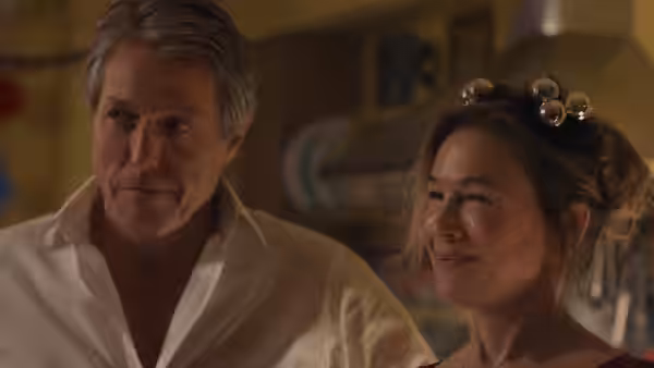 Daniel Cleaver (Hugh Grant) sitting beside a smiling woman indoors