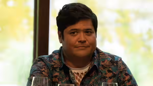 Eli (Harvey Guillén) seated at a table with wine glasses