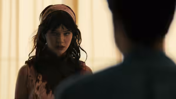 Iris (Sophie Thatcher) with blood on her dress facing a man indoors