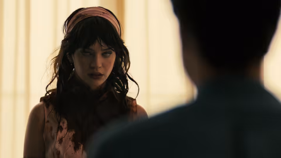 Iris (Sophie Thatcher) with blood on her dress facing a man indoors