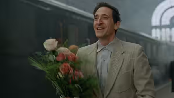a smiling man in a suit holds a bouquet at a station