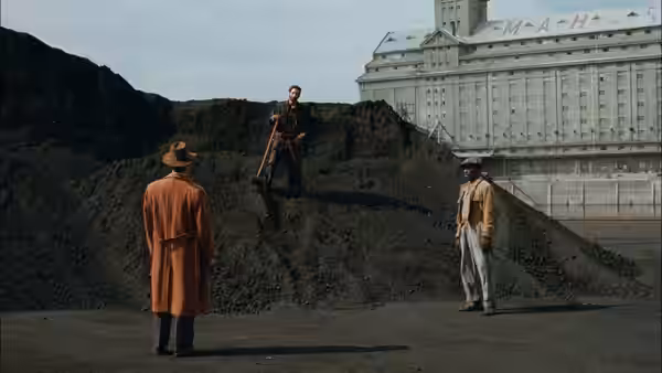 three men gather around a large dirt mound near a building