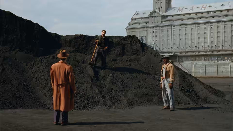 three men gather around a large dirt mound near a building