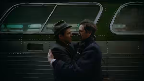 two men embrace beside a green train car