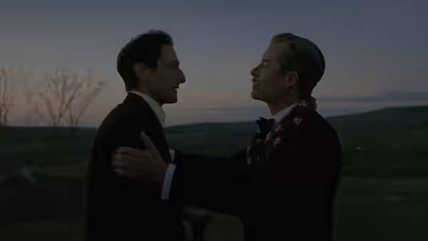 two men in formal suits embrace outdoors at dusk