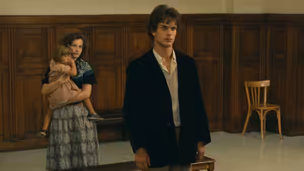 Yvon Targe (Christian Patey) stands in a wood-panelled room as a woman holds a child