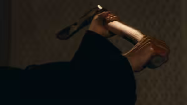 A hand grips a wooden-handled tool against a dim patterned wall