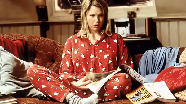 Bridget Jones (Renée Zellweger) sitting on a sofa reading a newspaper in pyjamas