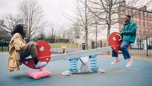 Yas (Vivian Oparah) and Dom (David Jonsson) playing on a seesaw in a playground