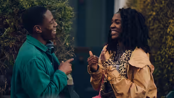 Dom (David Jonsson) and Yas (Vivian Oparah) laughing together outside a building