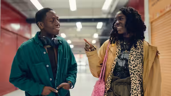 Dom (David Jonsson) and Yas (Vivian Oparah) walking and talking in an indoor corridor