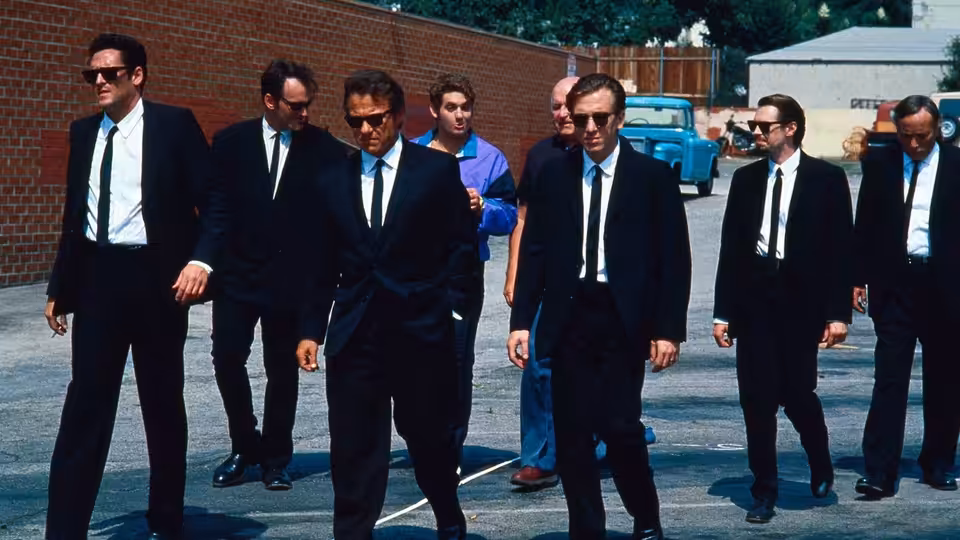 Men in black suits and ties walking across a parking lot