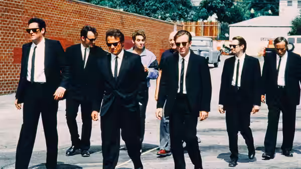 Men in black suits walking together in a sunlit parking lot