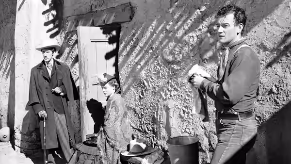 Man in dark shirt holds cloth near adobe wall with two others