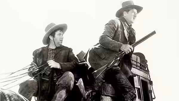 Two armed men ride atop stagecoach under bright open sky
