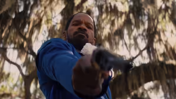 Django (Jamie Foxx) aiming a revolver upward in a moss-covered forest