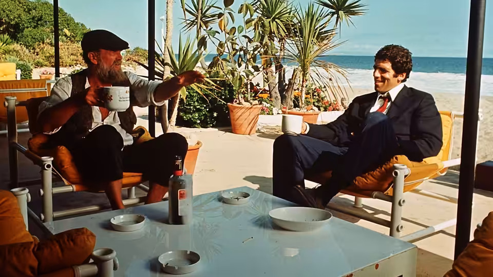 Roger Wade (Sterling Hayden) gestures while talking with Philip Marlowe on a sunny patio