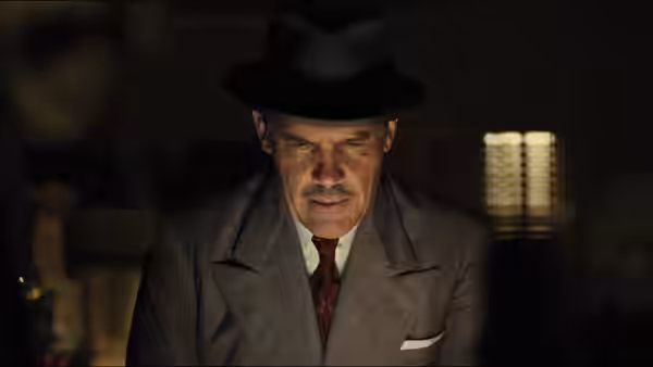 Eddie Mannix (Josh Brolin) in fedora and suit looks down in a dark room