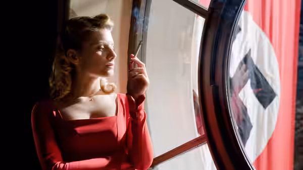Shosanna in a red dress smoking by a window with a swastika flag