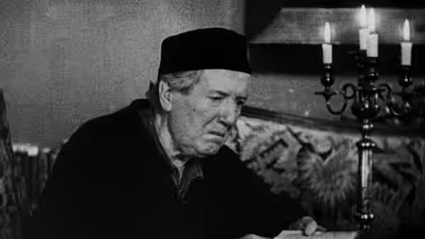 The Lord of the Manor (Maurice Schutz) sits beside a candlelit candelabrum
