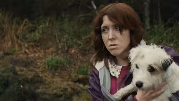 Tina (Alice Lowe) holding a small white dog in a forest clearing