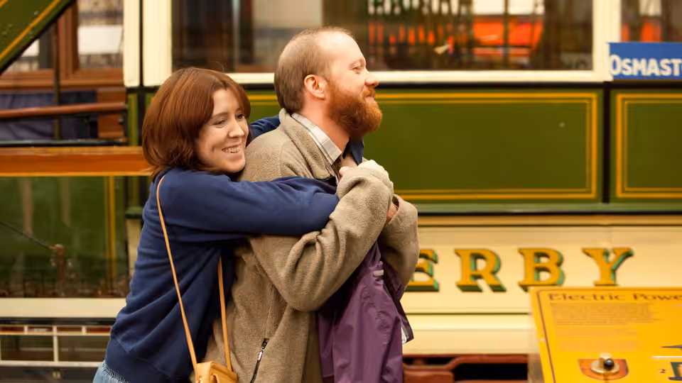 Tina (Alice Lowe) embracing Chris (Steve Oram) beside a green and yellow tram