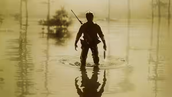 A soldier stands in shallow swamp water holding a rifle