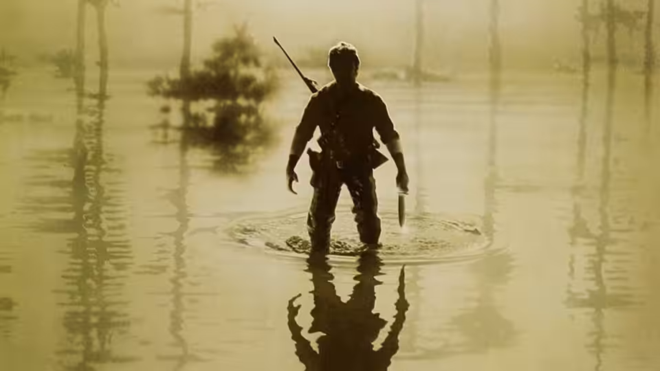 A soldier stands in shallow swamp water holding a rifle